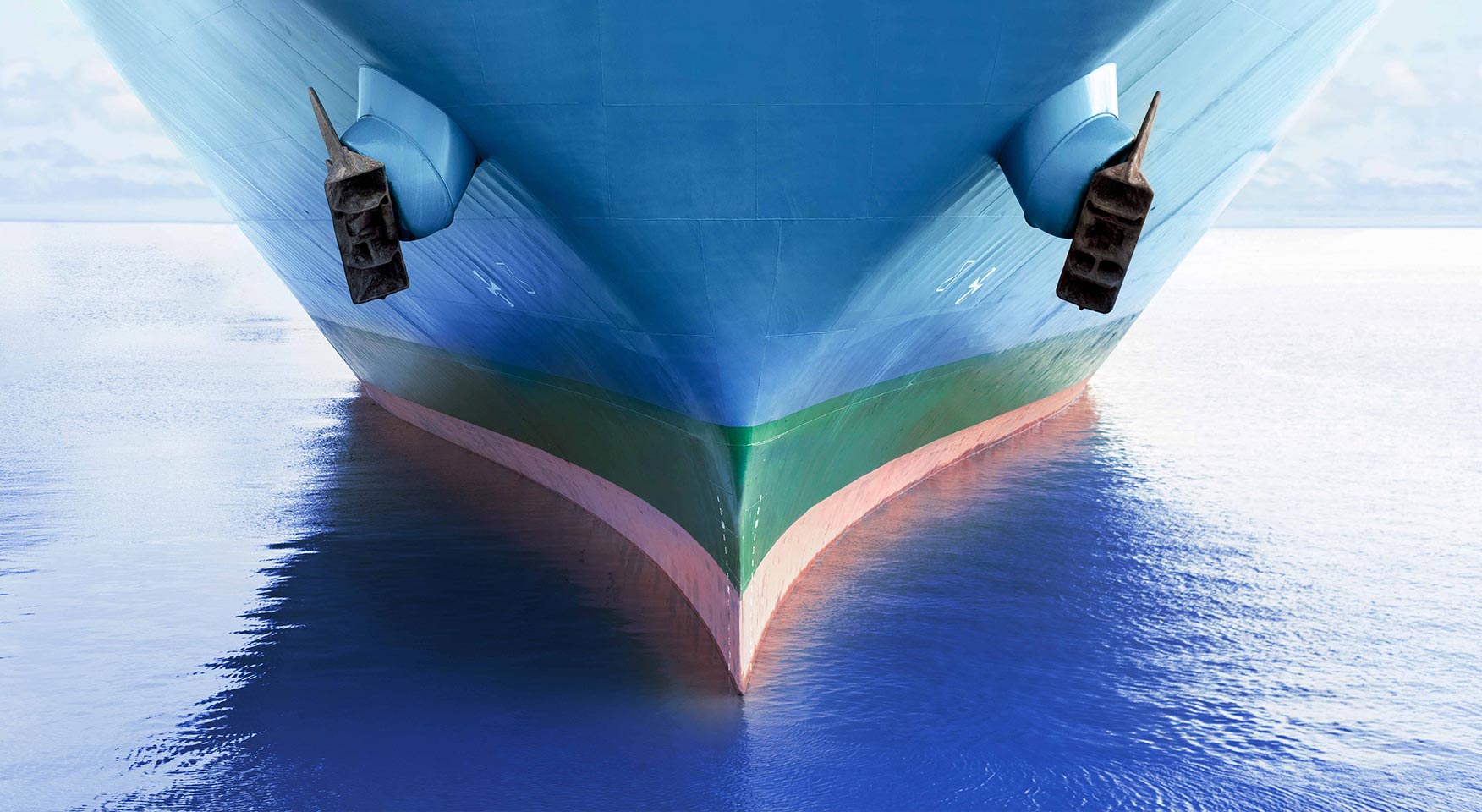 Vista frontale della prua di una grande nave cargo blu che naviga in mare calmo, con gli ancoraggi visibili ai lati dello scafo