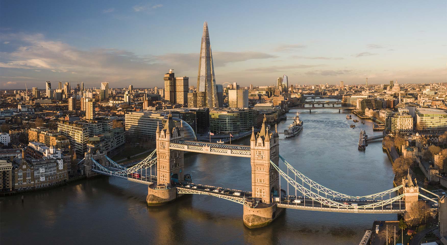 Vista panoramica dello skyline di Londra con Tower Bridge, il Tamigi e moderni grattacieli illuminati dalla luce del tramonto.